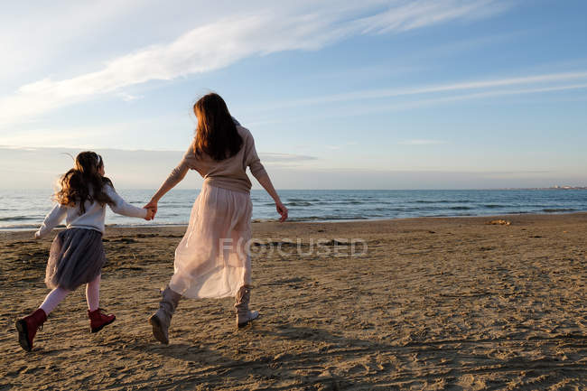 Вид ззаду матері з дочкою тримає руки під час прогулянки на пляжі — стокове фото