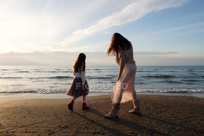 Вид ззаду матері з дочкою, що стоїть на пляжі проти неба з хмарами — стокове фото