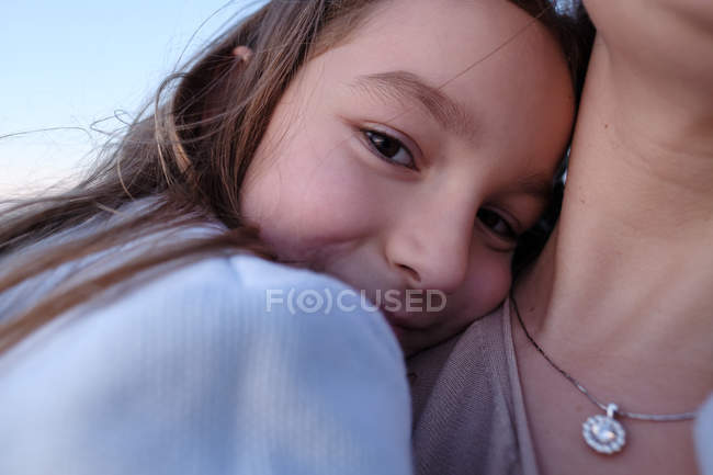 Дочка обіймає матір проти блакитного неба, фокус на передньому плані — стокове фото