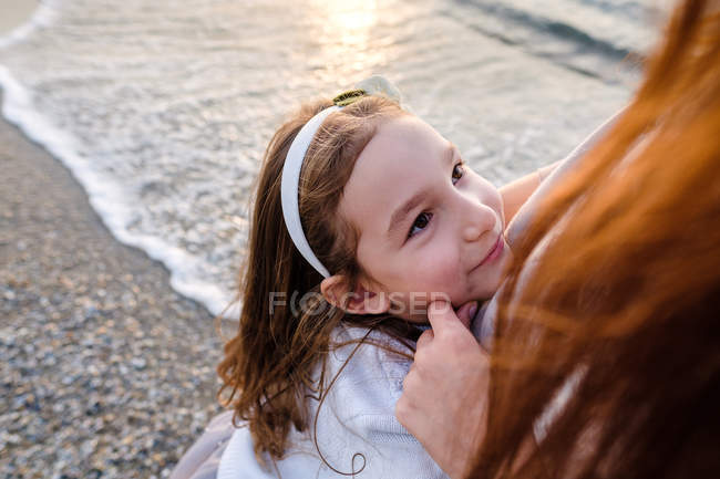 Hija abrazando a la madre contra la arena, enfoque en primer plano - foto de stock