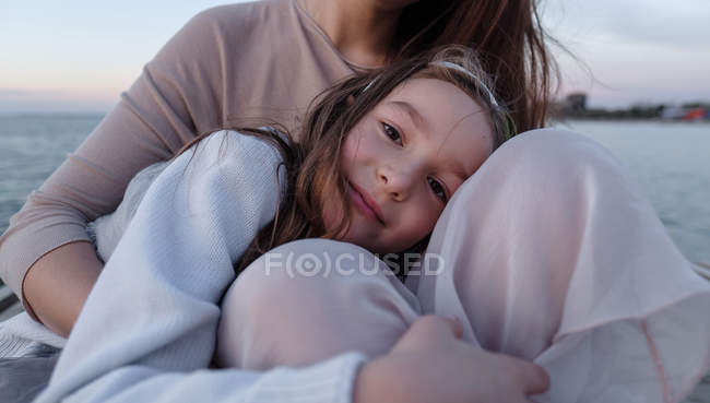 Filha abraçando mãe contra o mar, foco em primeiro plano — Fotografia de Stock