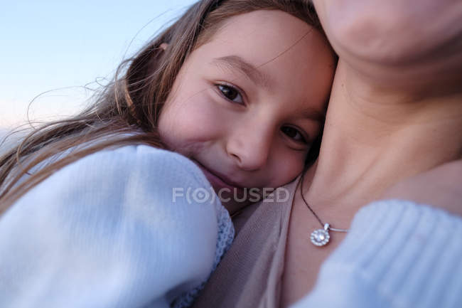 Daughter hugging mother against blue sky, focus on foreground — Stock Photo