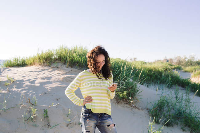 Молода жінка прослуховування музики з на пляжі, зосередити увагу на передньому плані смартфона — стокове фото