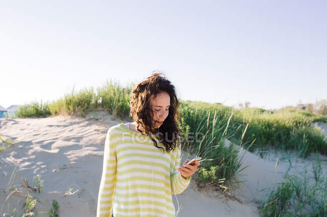 Jeune femme écoutant de la musique de smartphone à la plage, se concentrer sur l'avant-plan — Photo de stock