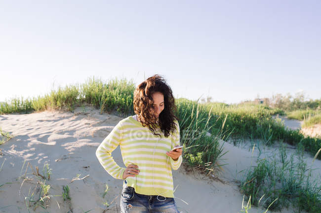 Молодая женщина слушает музыку со смартфона на пляже, сосредоточиться на переднем плане — стоковое фото