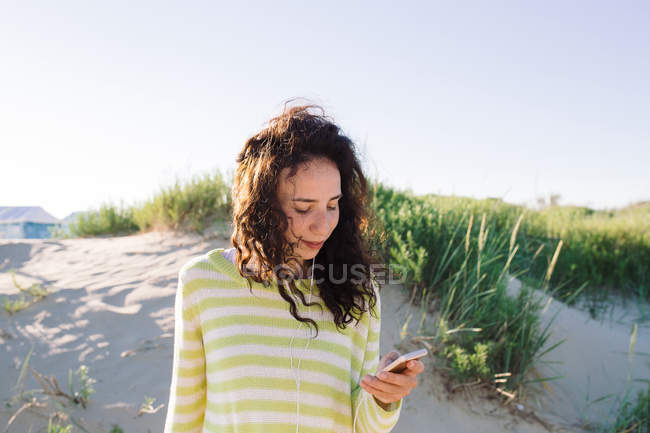 Jeune femme écoutant de la musique de smartphone à la plage, se concentrer sur l'avant-plan — Photo de stock