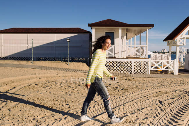 Vista lateral da jovem mulher ouvindo música na praia contra a construção — Fotografia de Stock