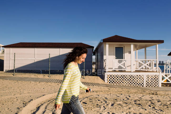 Vista laterale di giovane donna che ascolta musica sulla spiaggia contro edificio — Foto stock