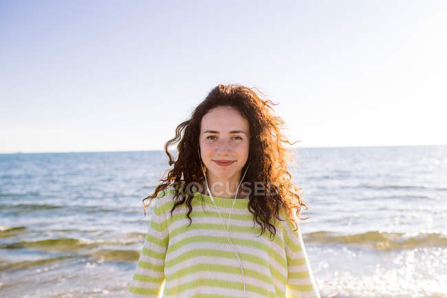 Щаслива молода жінка слухає музику на пляжі, фокус на передньому плані — стокове фото