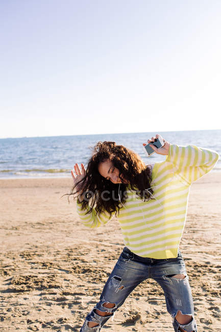 Donna con i capelli ricci ascoltare musica in spiaggia, concentrarsi sul primo piano — Foto stock