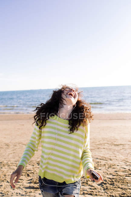 Жінка з кучерявим волоссям слухає музику на пляжі, фокус на передньому плані — стокове фото