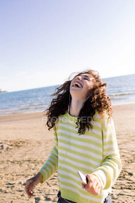 Donna con i capelli ricci ascoltare musica in spiaggia, concentrarsi sul primo piano — Foto stock