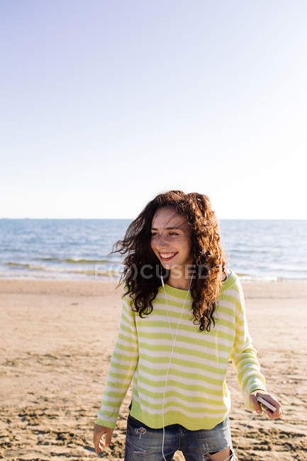 Жінка з кучерявим волоссям слухає музику на пляжі, фокус на передньому плані — стокове фото