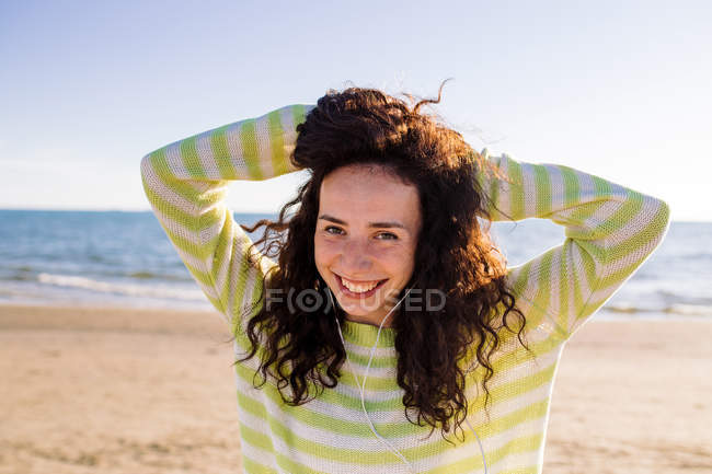 Сміється молода жінка з навушниками, слухаючи музику на пляжі, вибірковий фокус — стокове фото