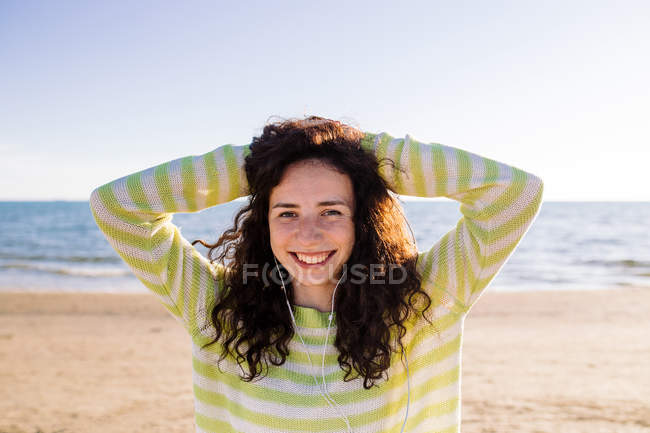 Lachende junge Frau mit Kopfhörern, die am Strand Musik hört, selektiver Fokus — Stockfoto