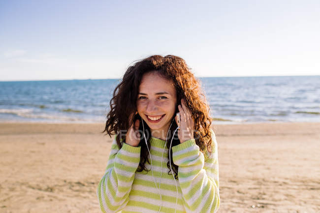 Сміючись молода жінка з навушники, прослуховування музики на пляжі, вибіркове фокус — стокове фото