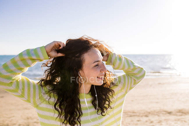 Lachende junge Frau mit Kopfhörern, die am Strand Musik hört, selektiver Fokus — Stockfoto