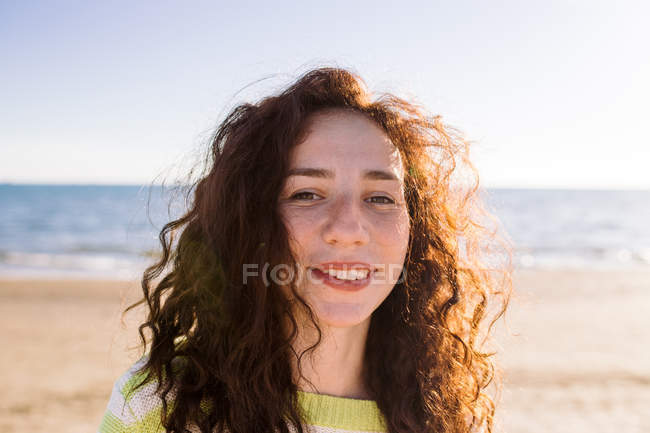 Portrait of beautiful woman with curly hair, sea in background — Stock Photo