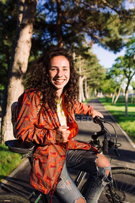 Junge Frau in orangefarbener Jacke auf Fahrrad sitzend, Fokus auf Vordergrund — Stockfoto