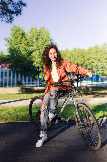 Jeune femme en veste orange assise à vélo, mise au premier plan — Photo de stock