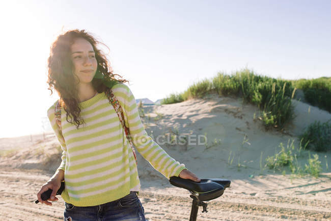 Attraente donna con bici contro la spiaggia, concentrarsi sul primo piano — Foto stock