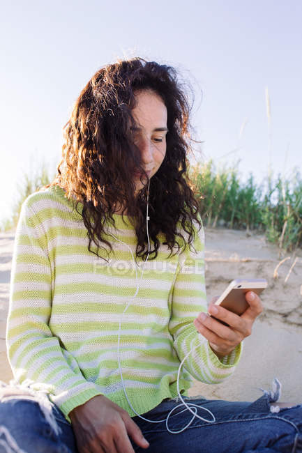 Young woman listening music from smartphone at beach, focus on foreground — Stock Photo