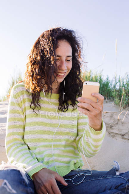Junge Frau hört am Strand Musik vom Smartphone, konzentriert sich auf den Vordergrund — Stockfoto