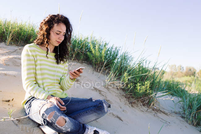 Молода жінка слухає музику зі смартфона на пляжі, фокус на передньому плані — стокове фото