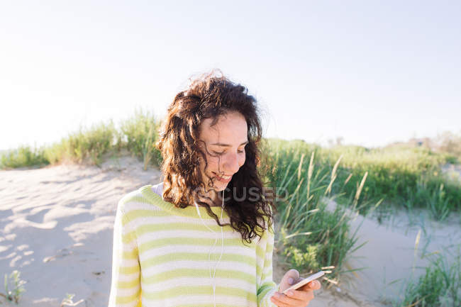 Junge Frau hört am Strand Musik vom Smartphone, konzentriert sich auf den Vordergrund — Stockfoto