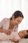 Happy young asian woman looking at her lovely baby sleeping on bed — Stock Photo