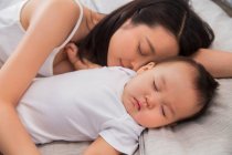 Hermosa joven asiático madre durmiendo con lindo bebé en casa - foto de stock