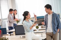 Усміхнена молода бізнес-леді тримає цифровий планшет і вказує пальцем під час розмови з чоловіком в офісі — стокове фото