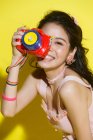 Bela feliz jovem asiático mulher segurando colorido câmera e sorrindo no amarelo — Fotografia de Stock