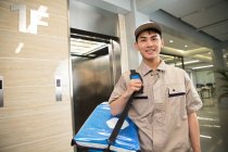 Bello giovani asiatico consegna uomo con borsa sorridente a fotocamera in ufficio — Foto stock
