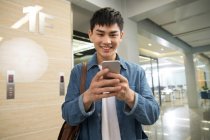 Sorridente giovane asiatico uomo utilizzando smartphone in ufficio — Foto stock