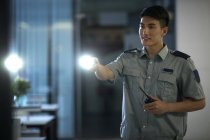 Souriant jeune garde de sécurité tenant lampe de poche et talkie-walkie dans le bureau la nuit — Photo de stock