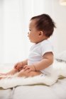 Side view of adorable asian baby sitting on bed at home — Stock Photo