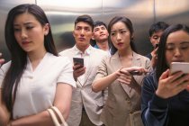 Занятой молодой азиат использует смартфоны в лифте — стоковое фото