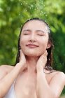 Primer plano vista de hermosa joven asiática tomando ducha con los ojos cerrados - foto de stock