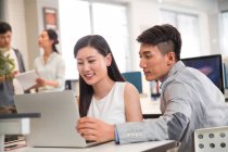 Smiling young asian businessman and businesswoman using laptop together in office — Stock Photo
