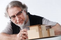 Серйозний професійний зрілий архітектор в окулярах, що працює з будівельною моделлю на робочому місці — стокове фото