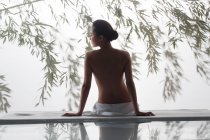 Rückseite der schönen nackten Frau sitzt auf Massagetisch im Wellnessbereich — Stockfoto