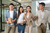 Професійні молоді азіатські бізнесмени та бізнес-жінки посміхаються на камеру під час прогулянки разом в офісі — стокове фото