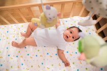 Vista superior de adorable asiático bebé acostado en cuna y mirando a la cámara, enfoque selectivo - foto de stock