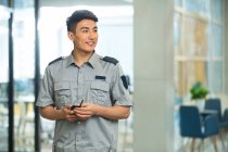 Sonriente joven guardia de seguridad sosteniendo walkie-talkie y mirando hacia otro lado en el centro de negocios - foto de stock