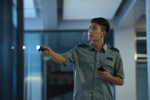Young asian security guard holding walkie-talkie and flashlight at night — Stock Photo