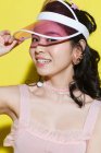 Красива щаслива азіатська дівчина регулює шапку і посміхається на камеру на жовтому — стокове фото