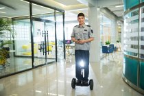 Smiling young security guard riding self-balancing scooter and using walkie-talkie in business center — Stock Photo