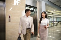 Feliz jovem asiático empresário e empresária sorrindo uns aos outros enquanto caminhando juntos no escritório — Fotografia de Stock