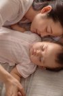 Вид сверху на красивую молодую маму и восхитительного младенца, спящего вместе на кровати — стоковое фото